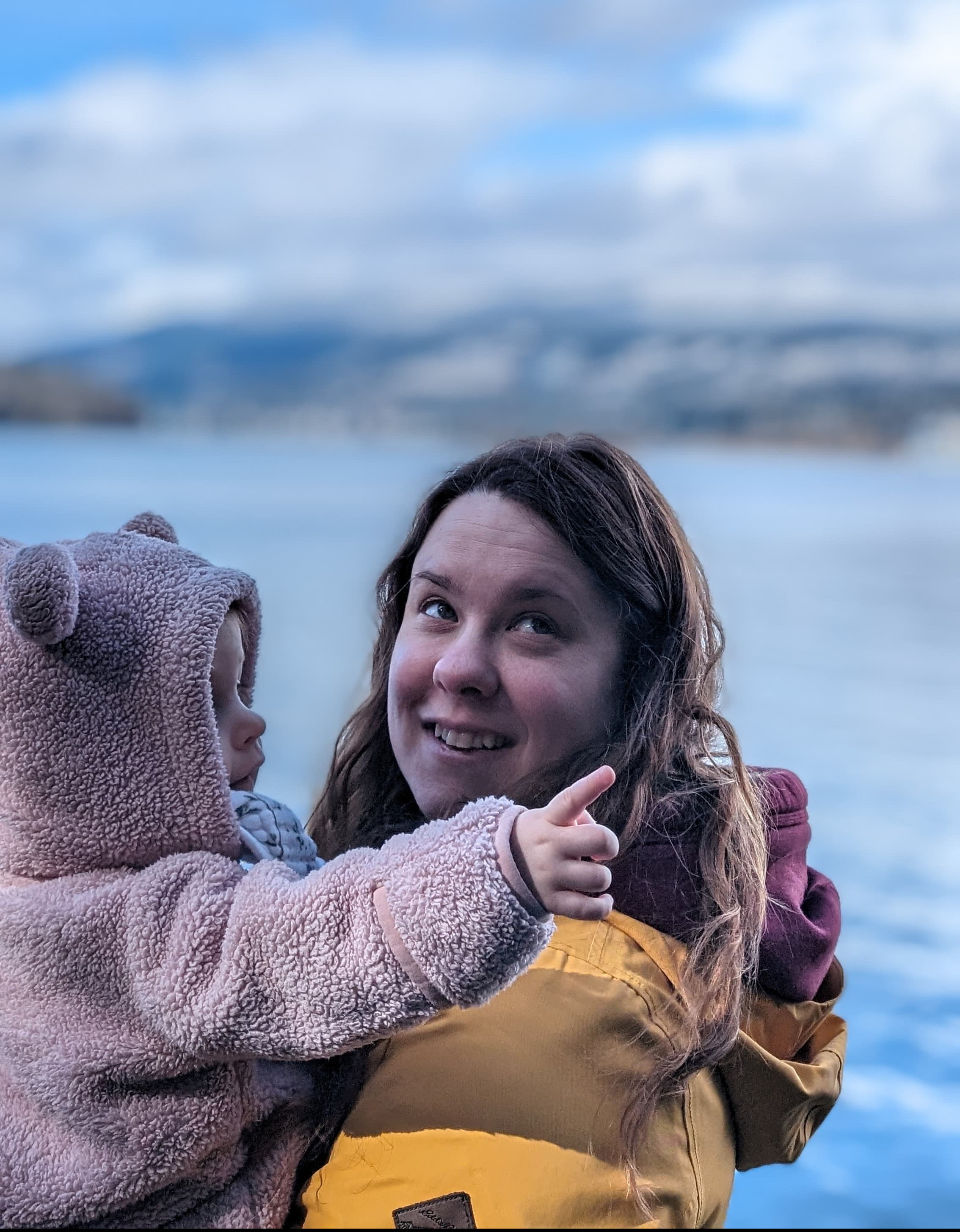 Woman holding a toddler. The toddler is pointing upwards and the woman is looking in that direction