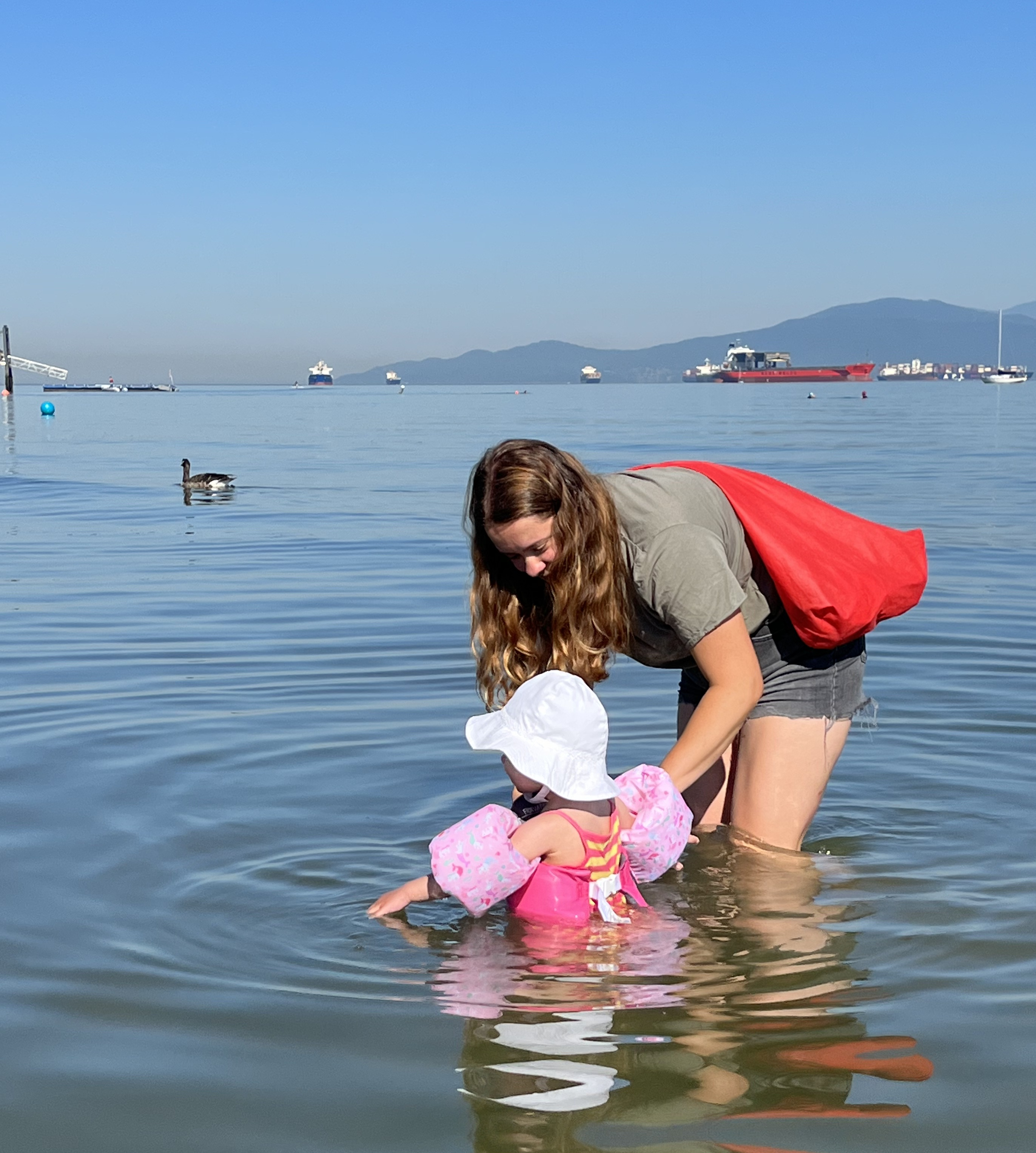 Woman holding a toddler while wading in the ocean