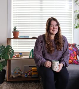 Woman sitting on a couch holding coffee and smiling at the camera