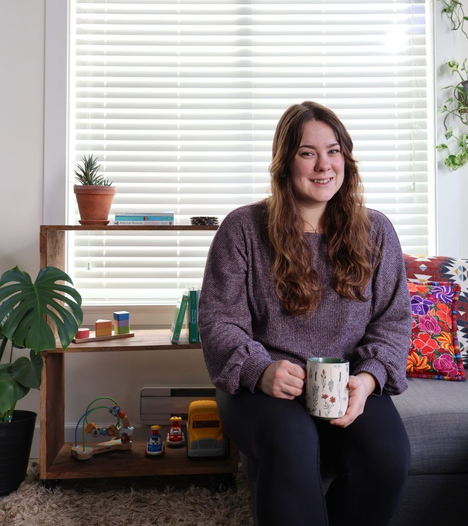 Woman sitting on a couch holding coffee and smiling at the camera