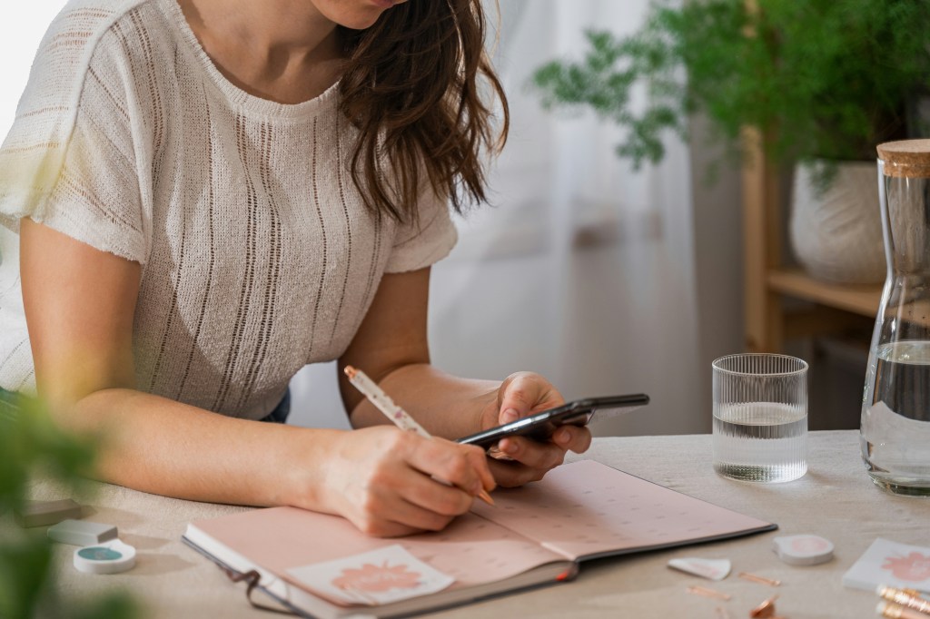 Woman holding a phone and a pencil, taking notes