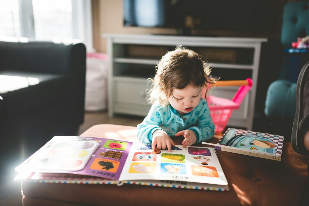 toddler reading a picture book at a low table in their living room